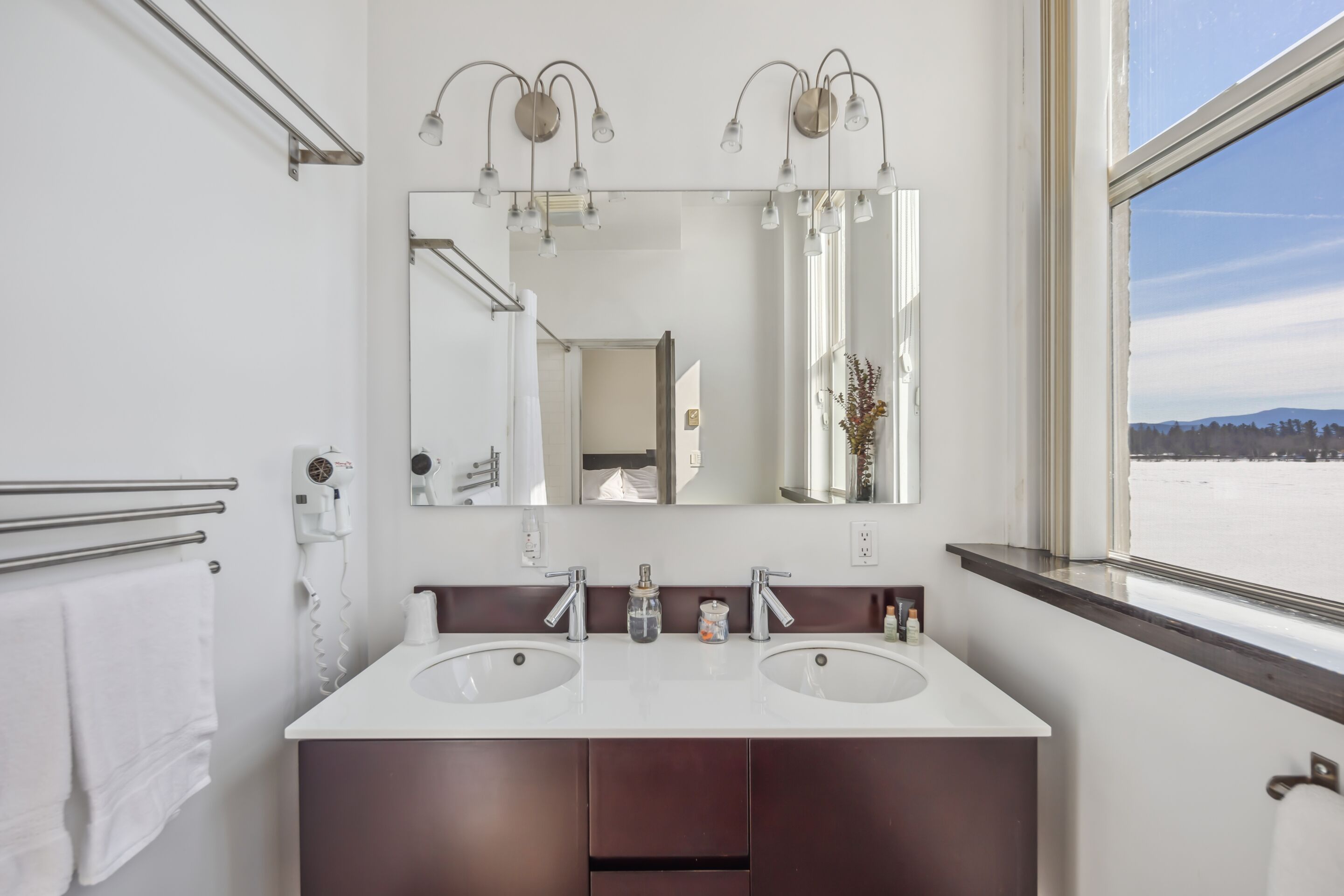 A bathroom with two sinks, a large mirror, and a window with a view of a snowy landscape.
