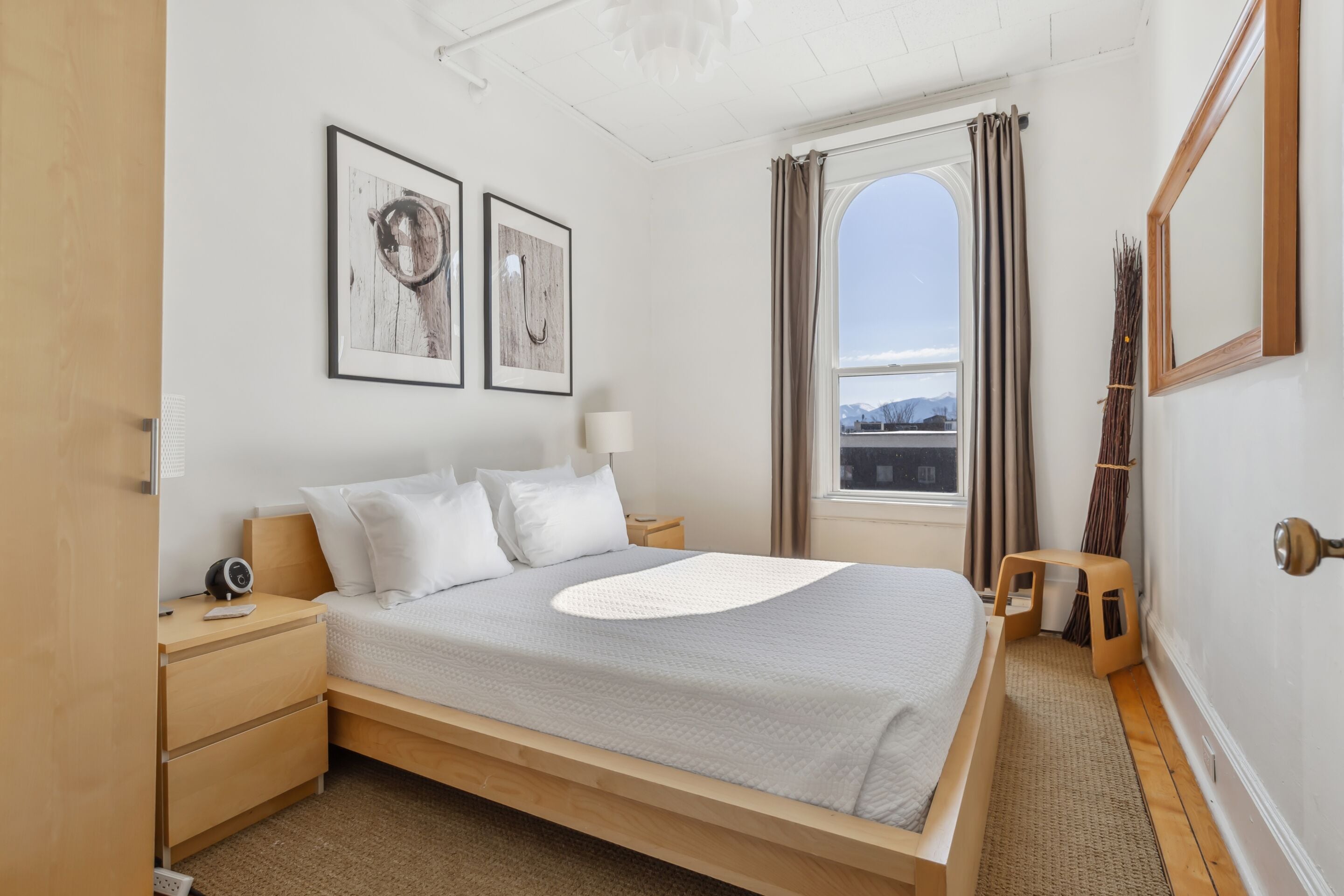 A bedroom with a bed, bedside tables, a nightstand, a window with curtains, and framed pictures on the wall.