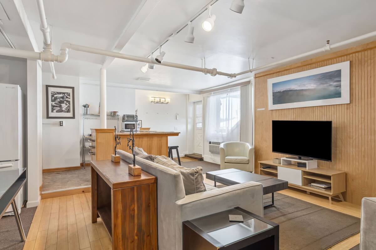 Un salon moderne avec un meuble TV en bois, un grand téléviseur à écran plat, un canapé et un coin repas comprenant une table et des chaises en bois.