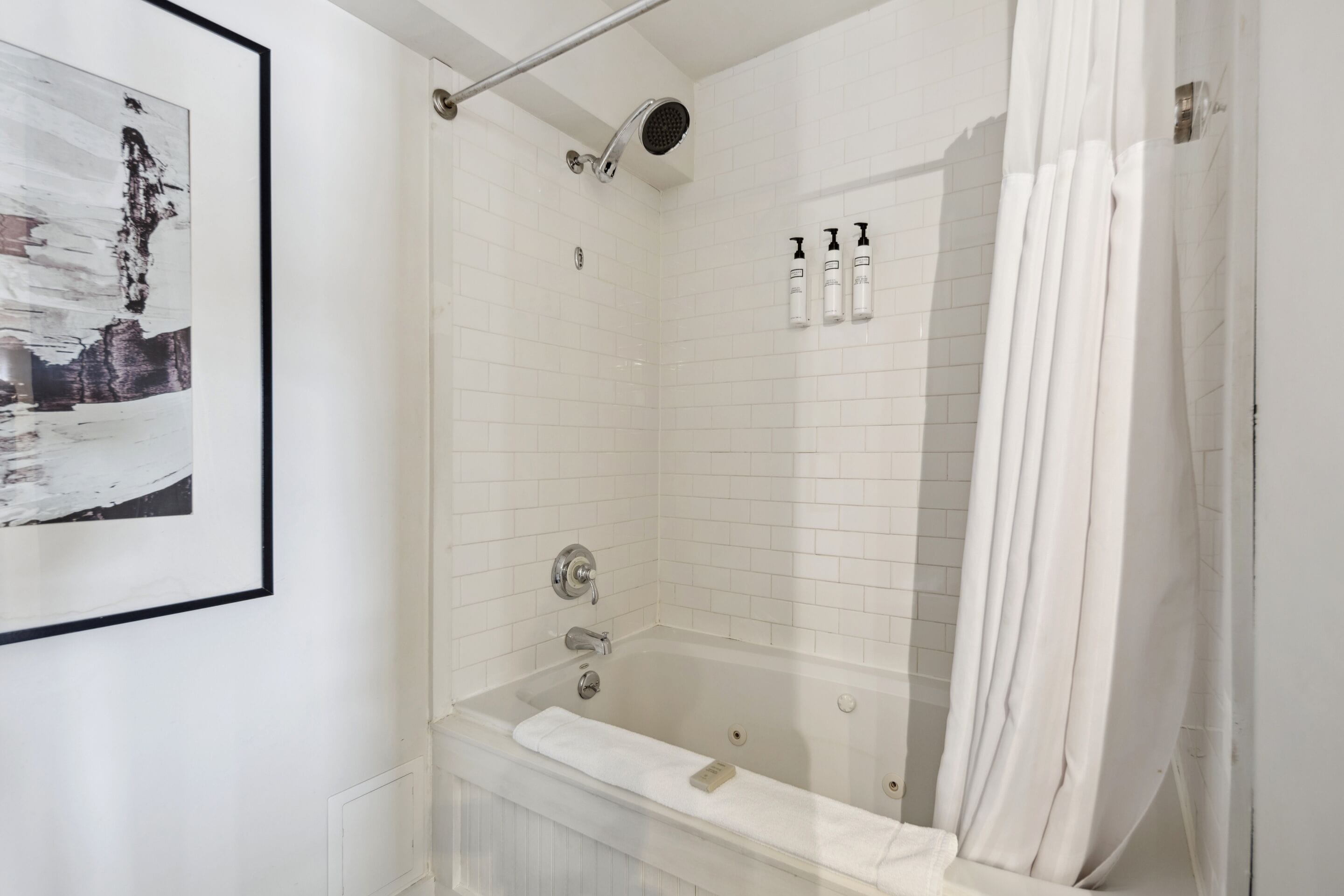 A modern bathroom with a glass-enclosed shower, white tiled walls, and a framed picture on the wall.
