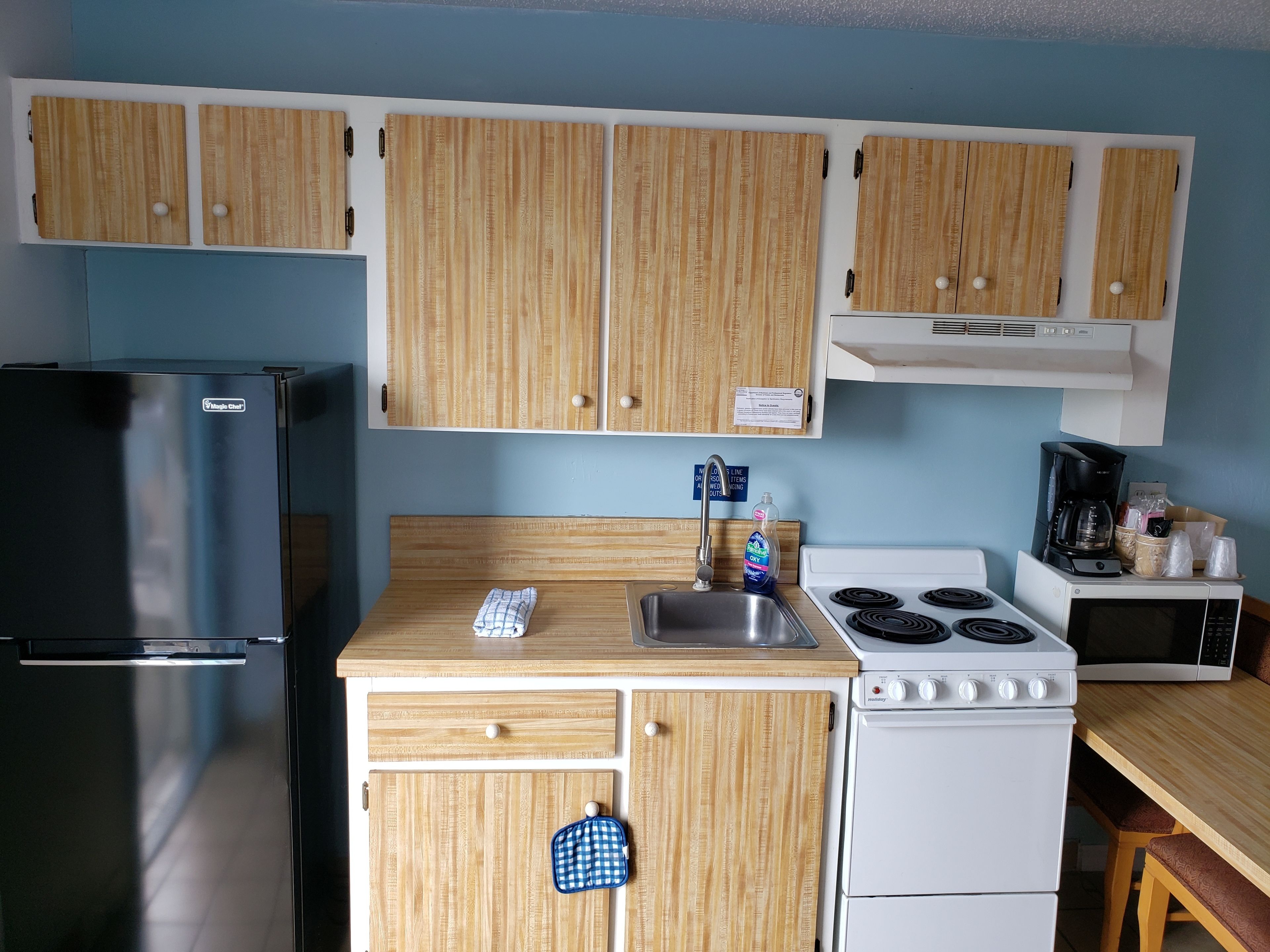 Una cocina compacta con armarios de madera, un refrigerador de acero inoxidable, una estufa y un microondas.