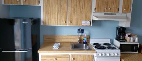 Una cocina compacta con armarios de madera, un refrigerador de acero inoxidable, una estufa y un microondas.