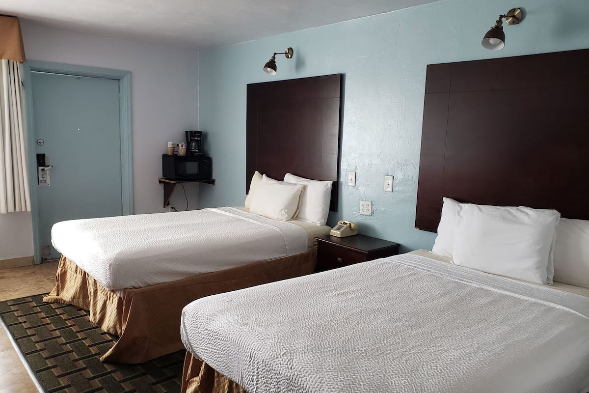 A hotel room with two beds, a bedside table with a phone, a coffee maker, and a wall-mounted lamp.