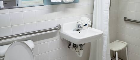 A bathroom with a toilet, sink, and shower area. There are towels and a green bottle on a shelf.
