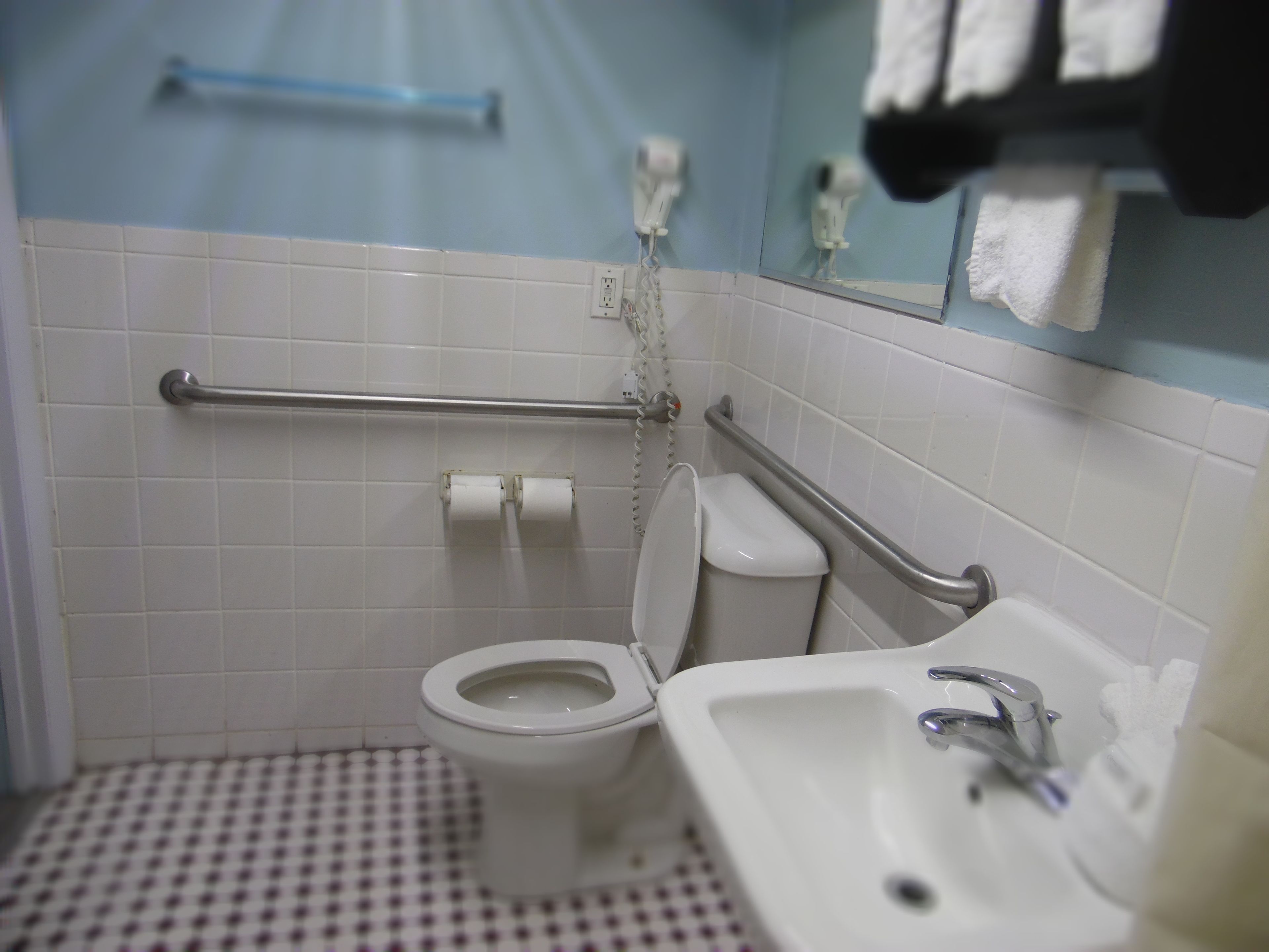 Baño con inodoro, lavamanos y barras de apoyo.