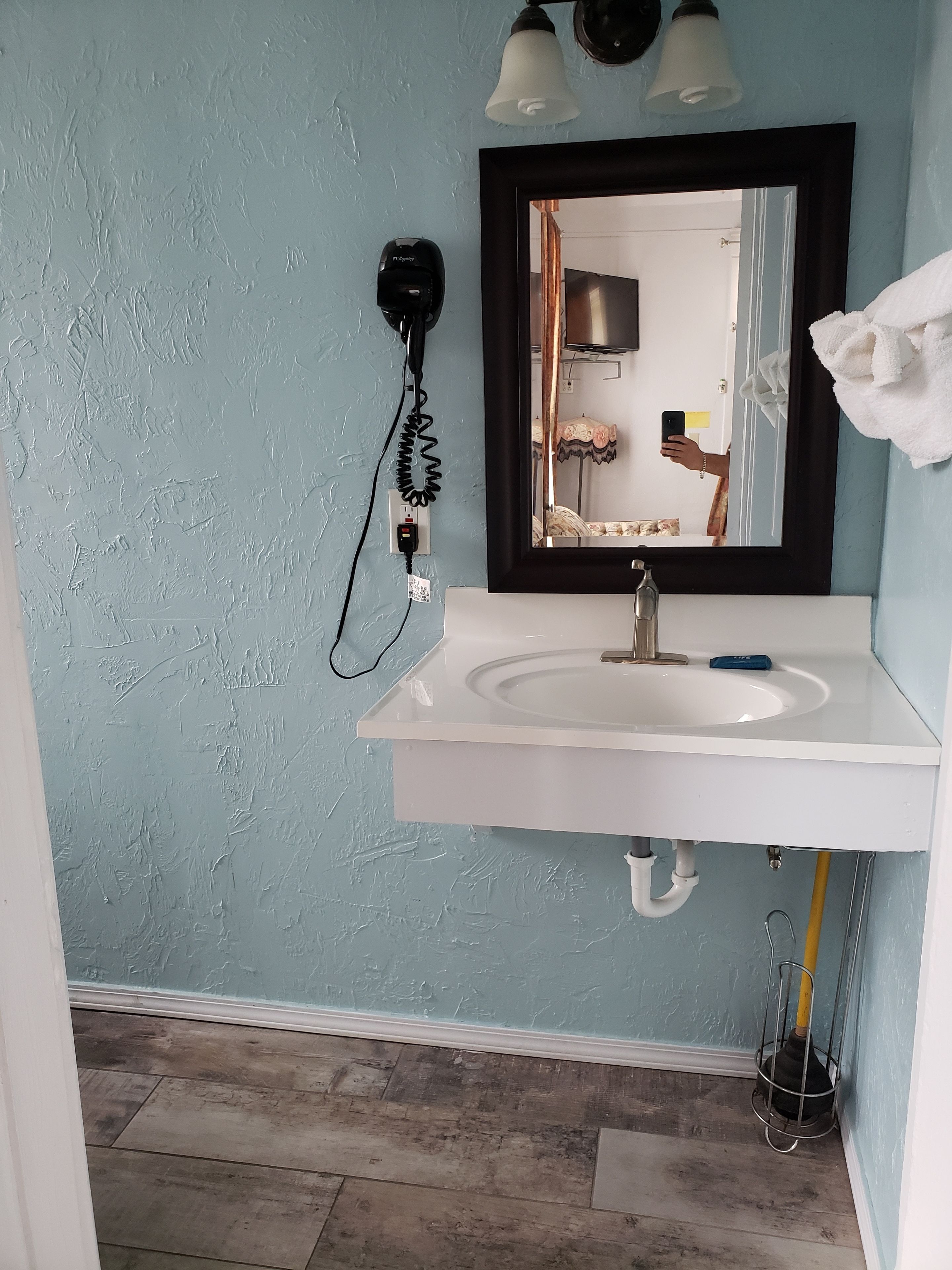 A bathroom with a white sink, a black wall-mounted mirror, and a towel hanging on the wall.
