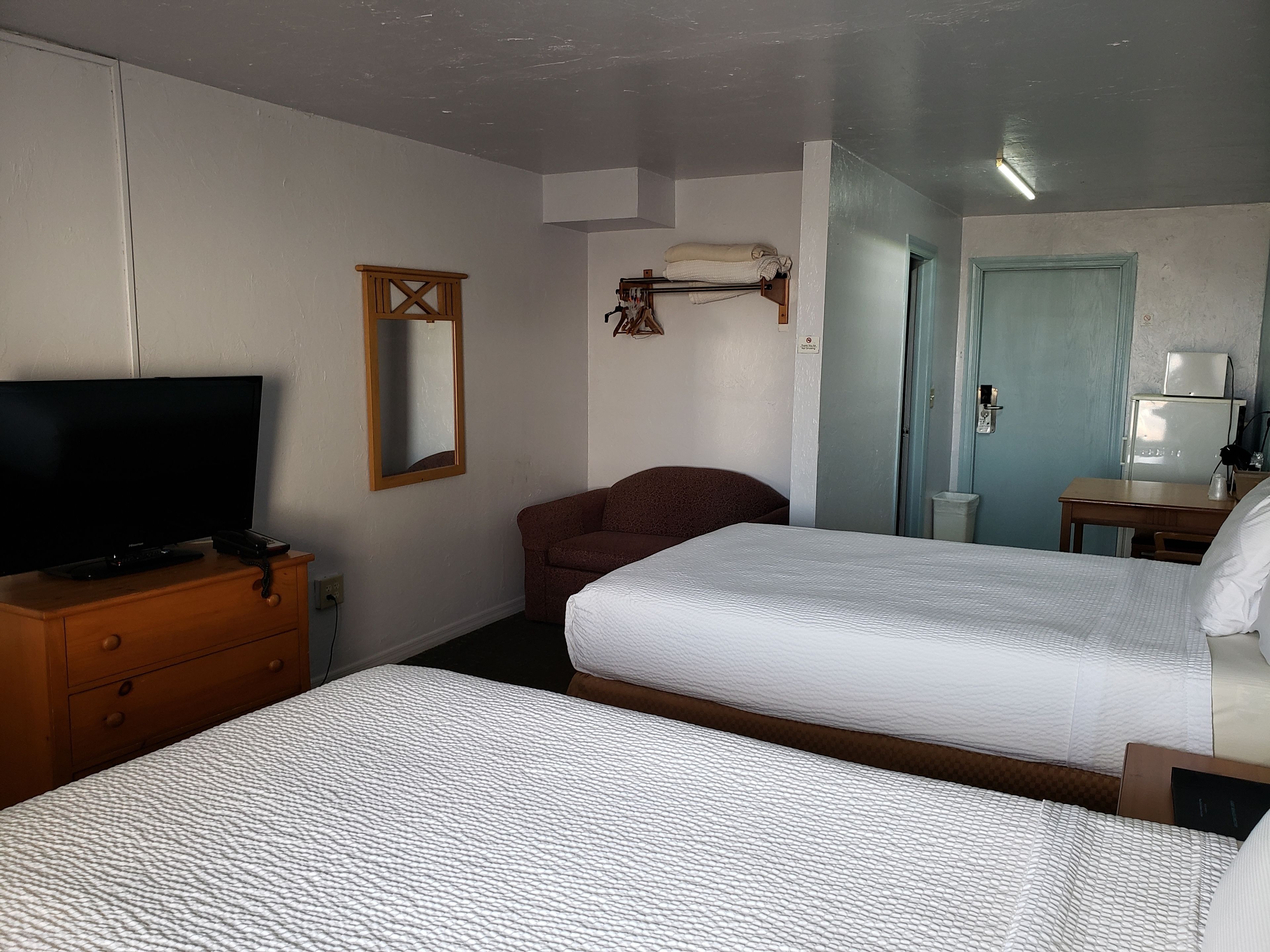 A hotel room with two beds, a TV on a wooden dresser, a mirror, and a small table with a lamp.