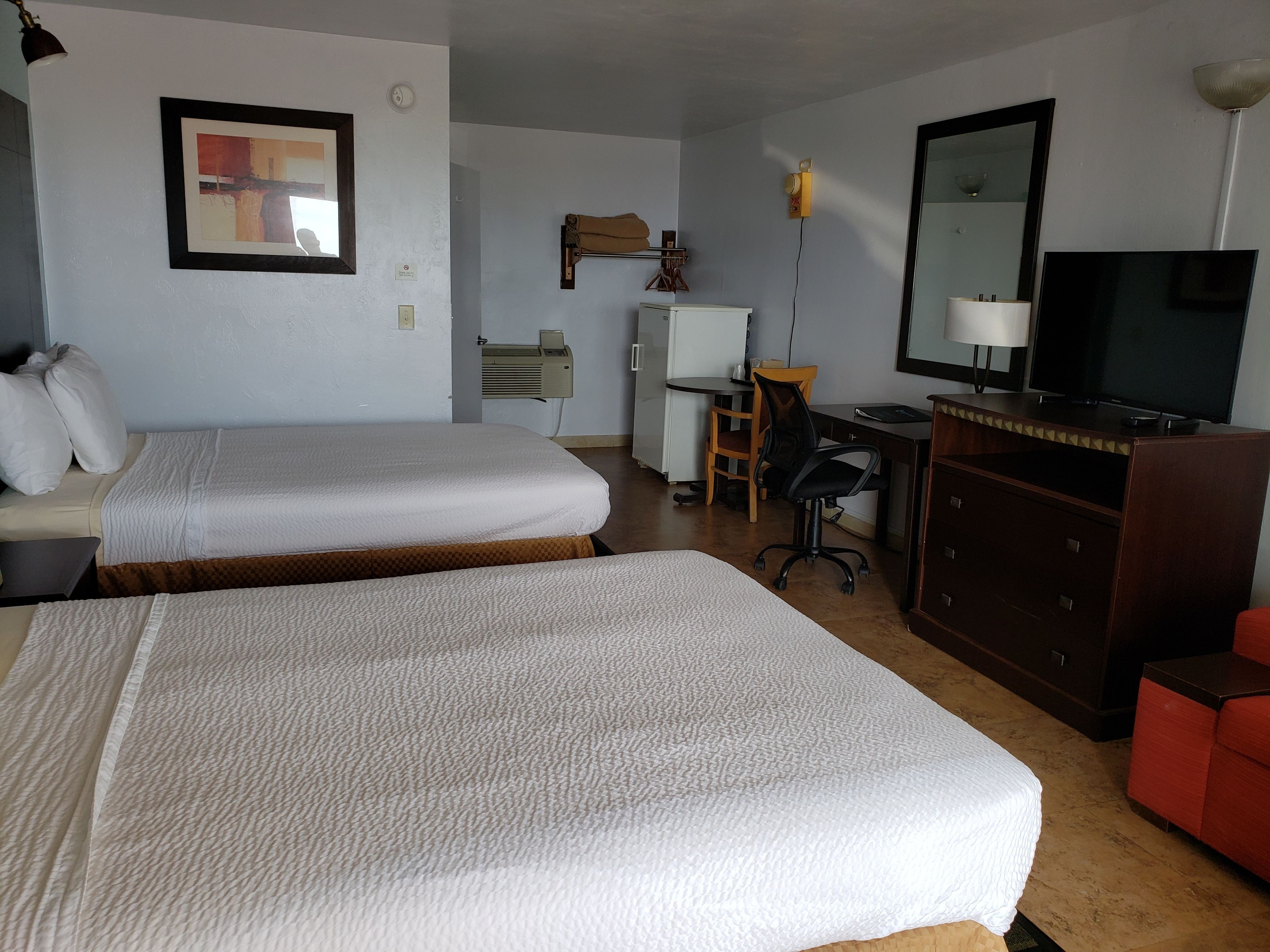 A hotel room with two beds, a desk with a chair, a television, and a dresser.