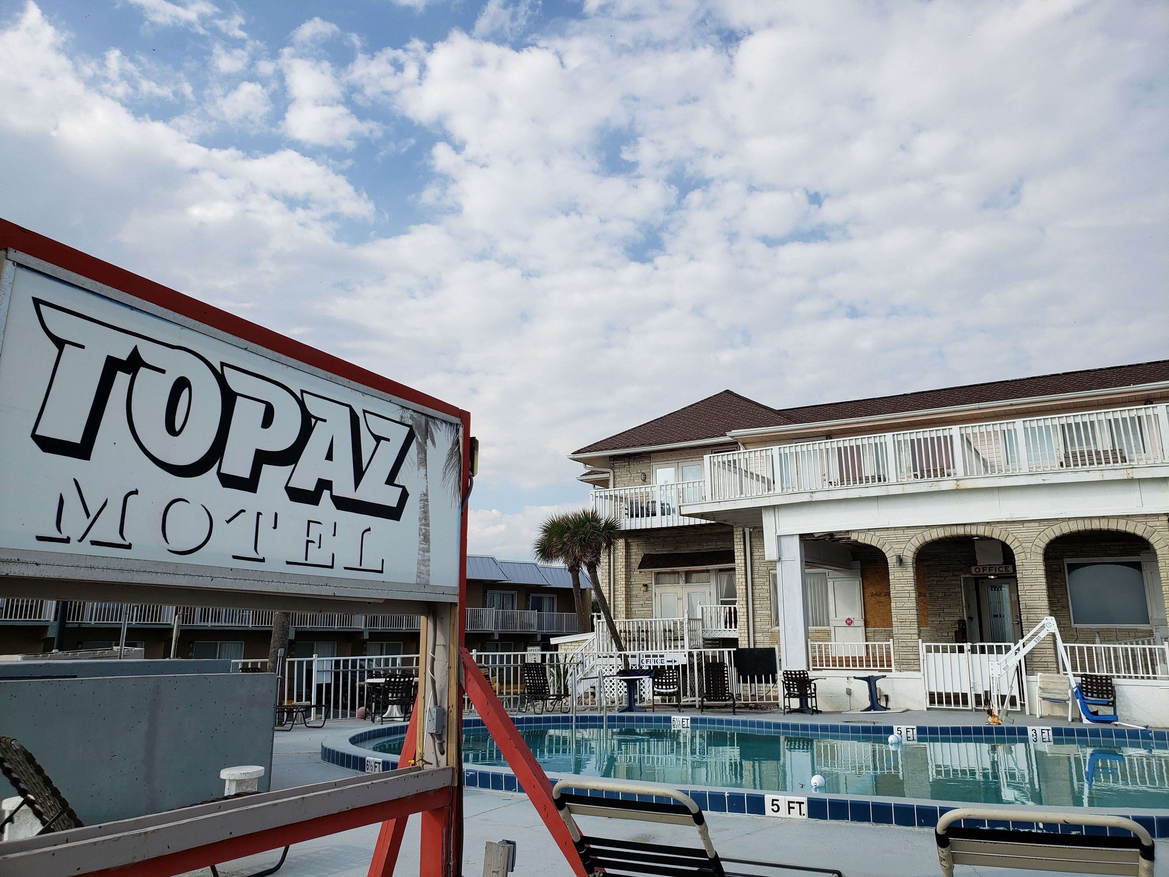 A motel with a pool, outdoor seating, and a sign reading "TOPAZ MOTEL".