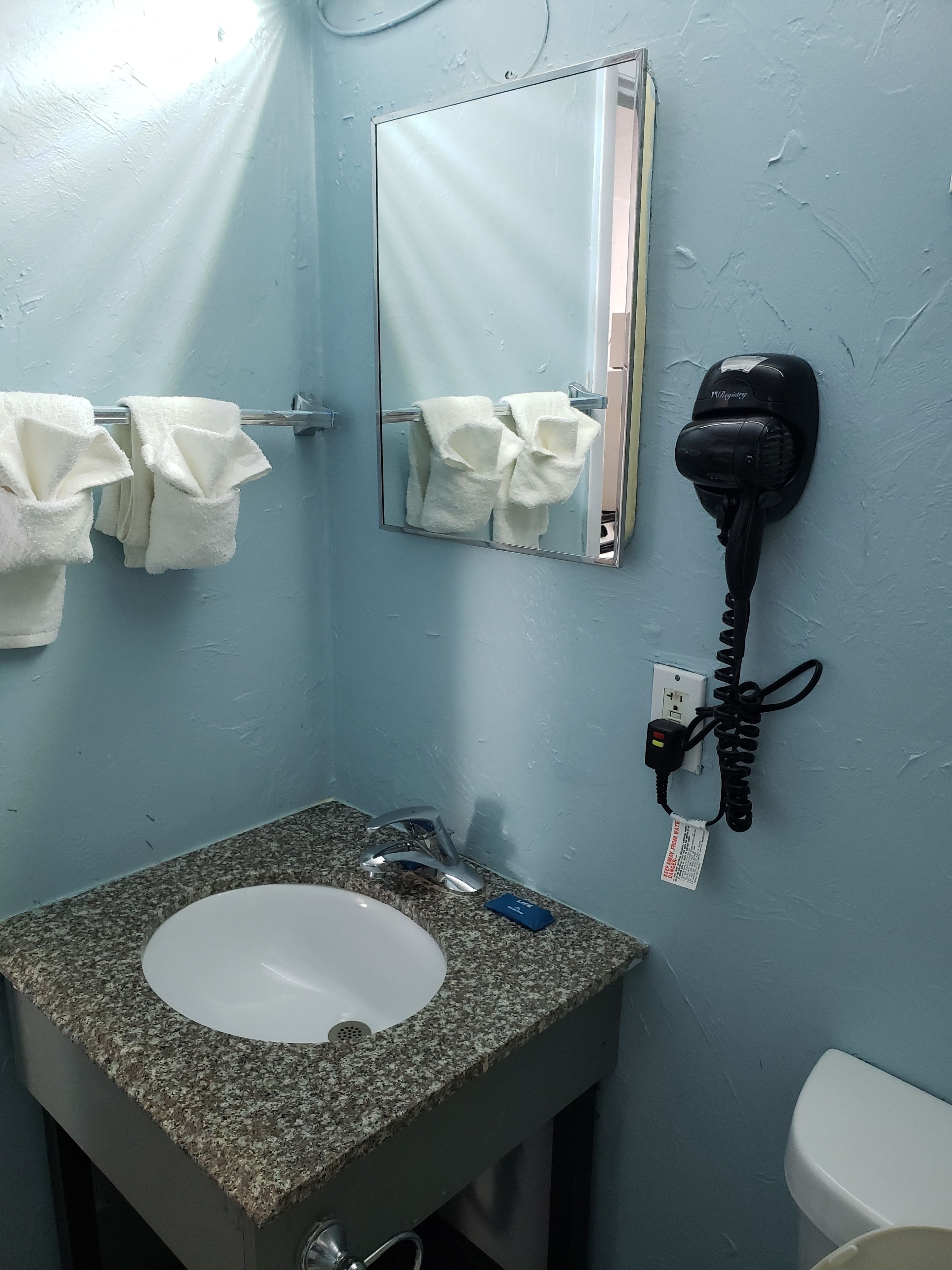 A bathroom with a granite countertop sink, a mirror, and a hairdryer mounted on the wall.