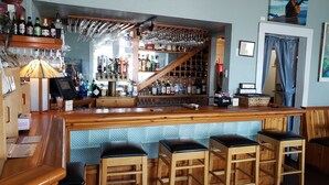 A bar area with wooden stools, a bar counter, and shelves stocked with bottles. - Topaz Motel (Flagler Beach)