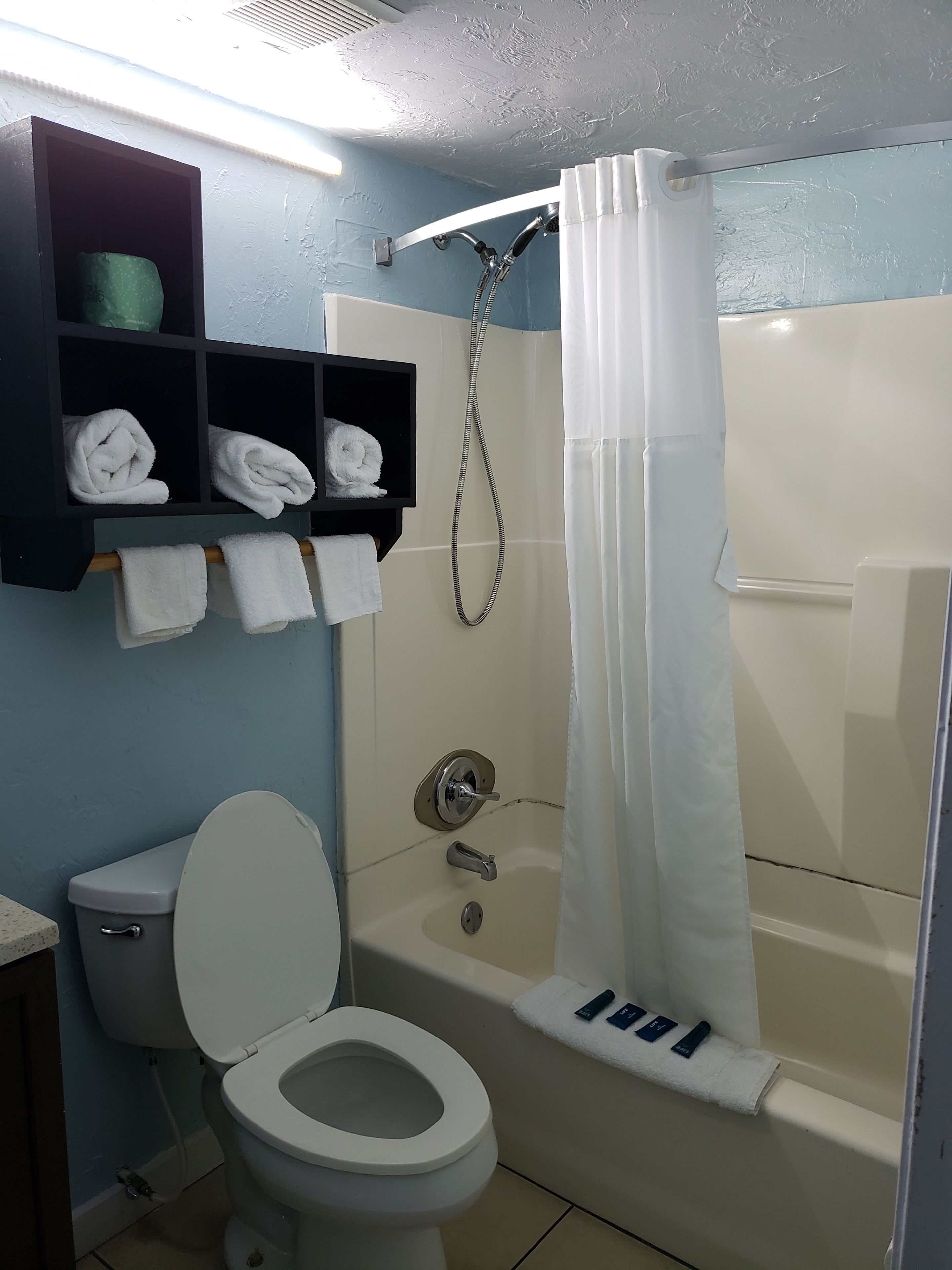 A bathroom with a toilet, a shower with a curtain, and shelves with towels.