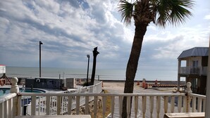 A beach view from a wooden deck with a pool, palm tree, and a sign for a motel. - Topaz Motel (Flagler Beach)