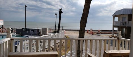 Vista de una playa desde una terraza de madera con piscina, palmera y un letrero de motel.
