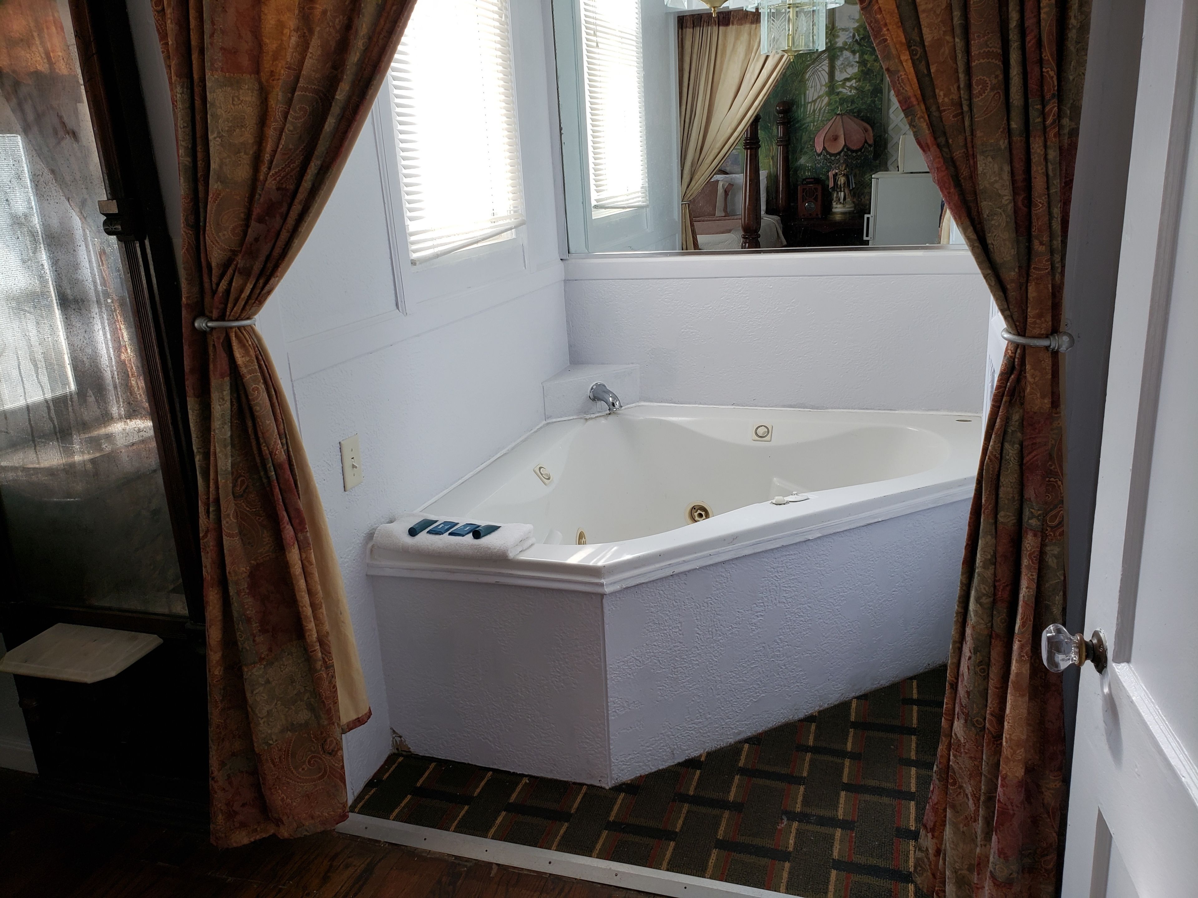 Ein Badezimmer im Eckbereich mit einer weißen Badewanne, einem kleinen Fenster mit Jalousien und einer Duschkabine.