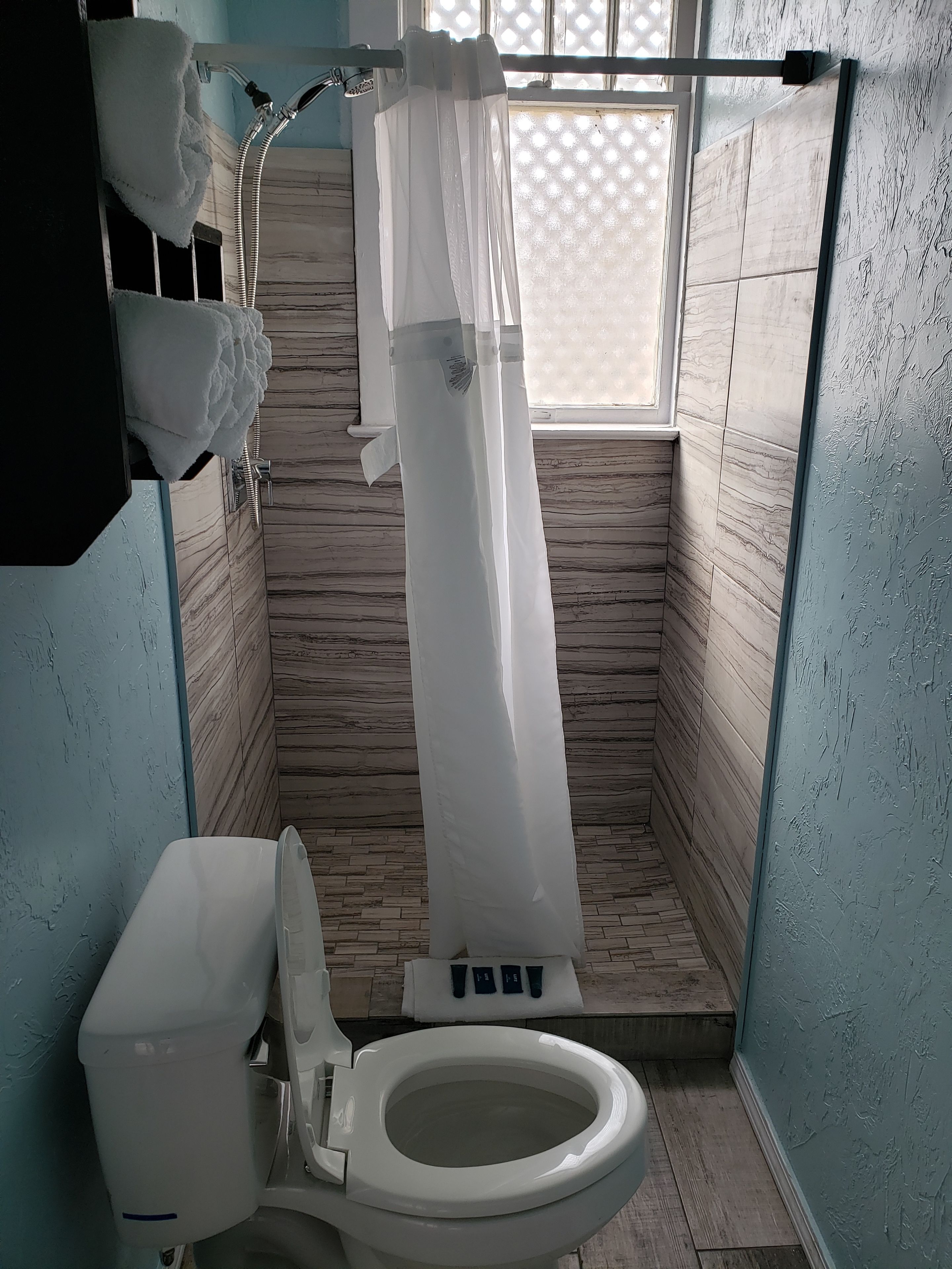 Et badeværelse med toilet, badeforhæng og et vindue med et gittermønster.