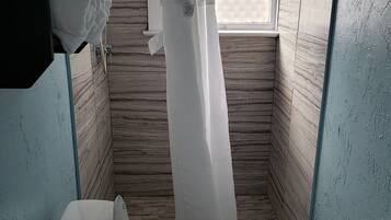Une salle de bain avec des toilettes, un rideau de douche et une fenêtre ornée d’un motif en treillis.