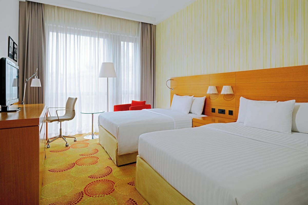 A hotel room with two beds, a desk, a chair, and a TV.