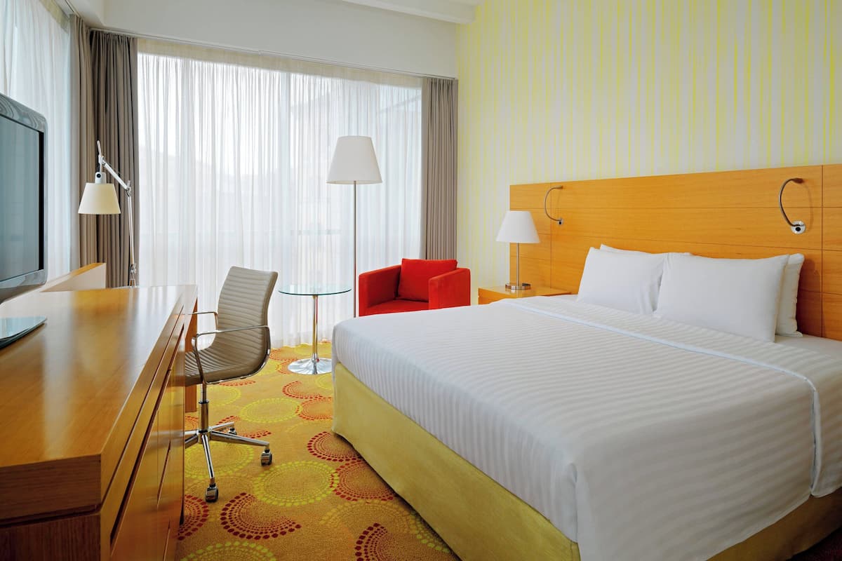 A hotel room with a large bed, a desk with a chair, a television, and a lamp.