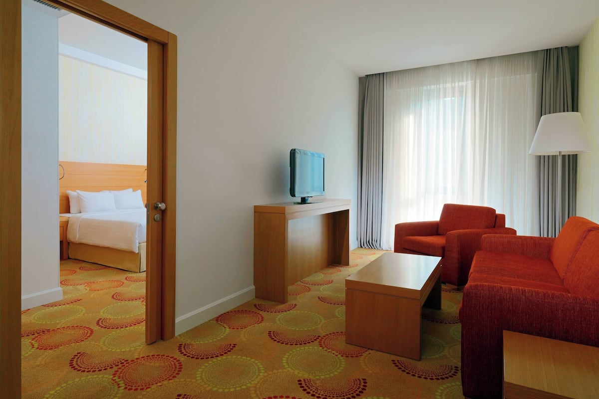 A hotel room with a bed, a TV on a stand, a sofa, a coffee table, and a lamp.
