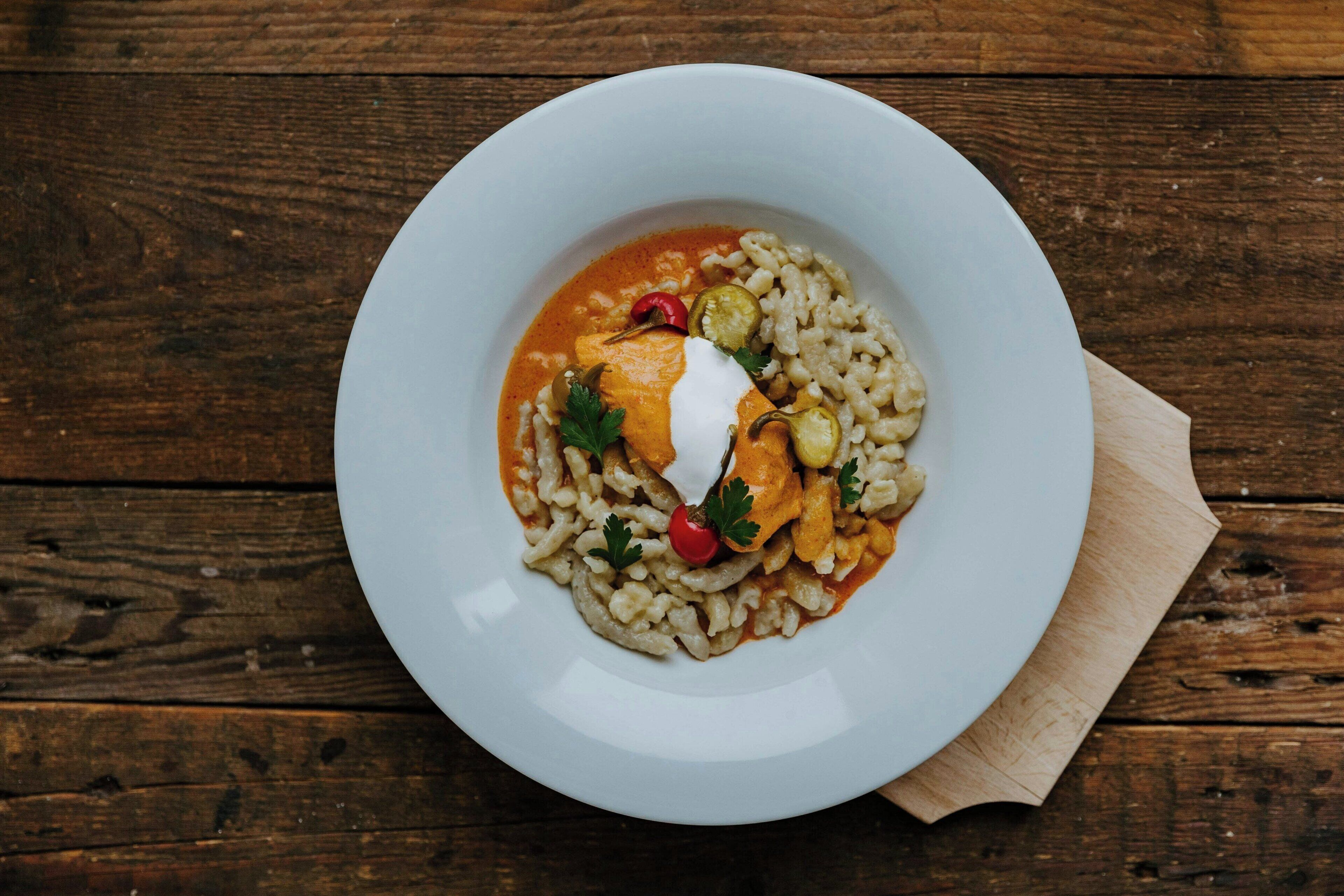Un plato blanco con pasta, coronado por una cucharada de crema, una rodaja de tomate y un adorno.