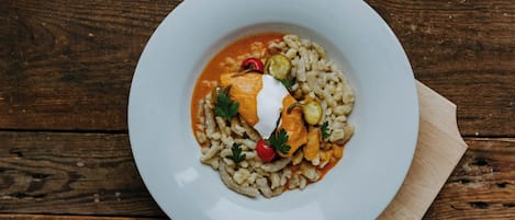 Un plato blanco con pasta, coronado por una cucharada de crema, una rodaja de tomate y un adorno.