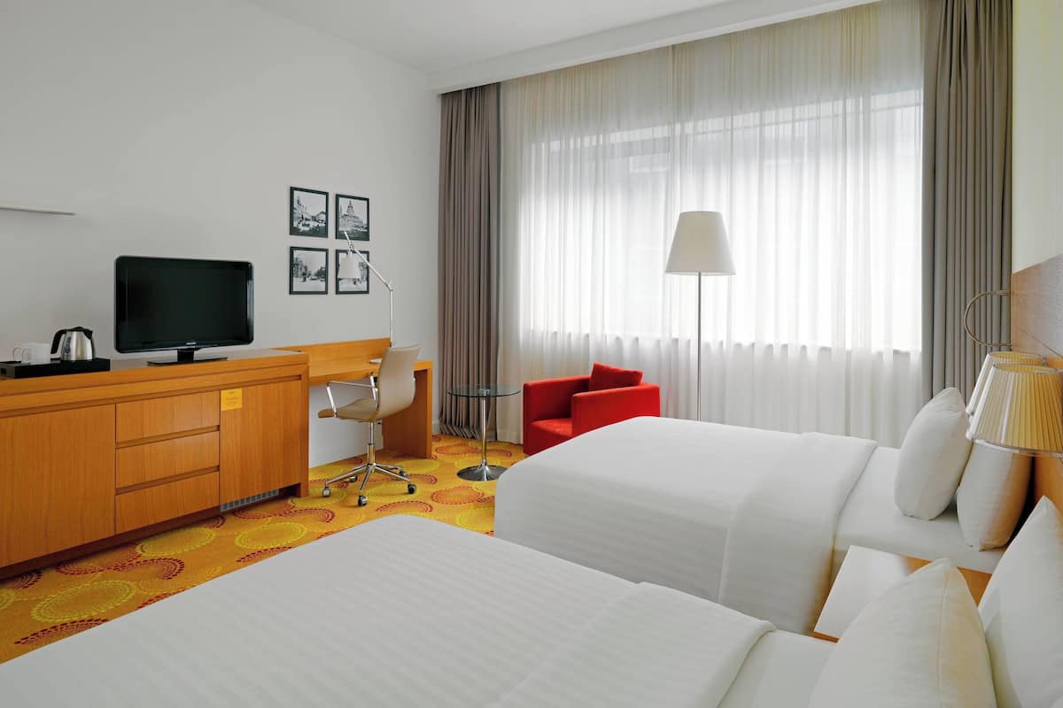 A hotel room with two beds, a desk with a TV, a chair, and a red sofa.