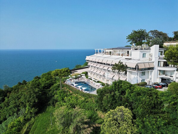 A coastal hotel with a pool, multiple balconies, and a view of the sea. - Posillipo (Gabicce Mare)