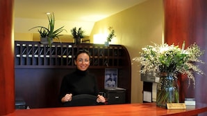 A reception desk with a wooden finish, a potted plant, and a vase with flowers. - Kyriad - Caen Centre (Caen)