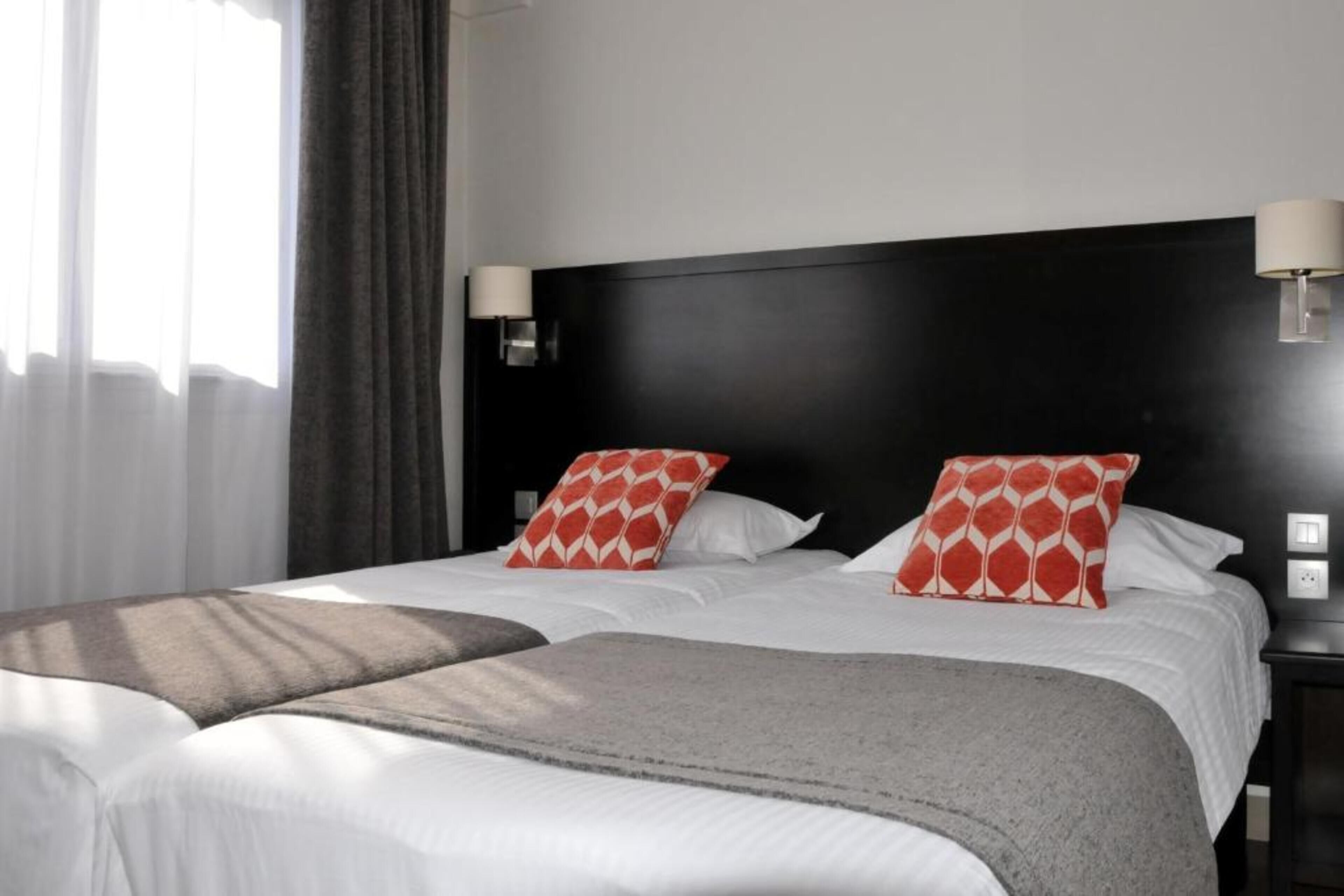Una habitación de hotel con una cama grande, dos mesitas de noche y un ventanal con cortinas.