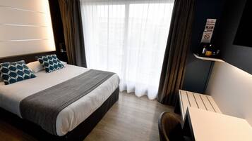 A hotel room with a bed, a desk, and a window with curtains.