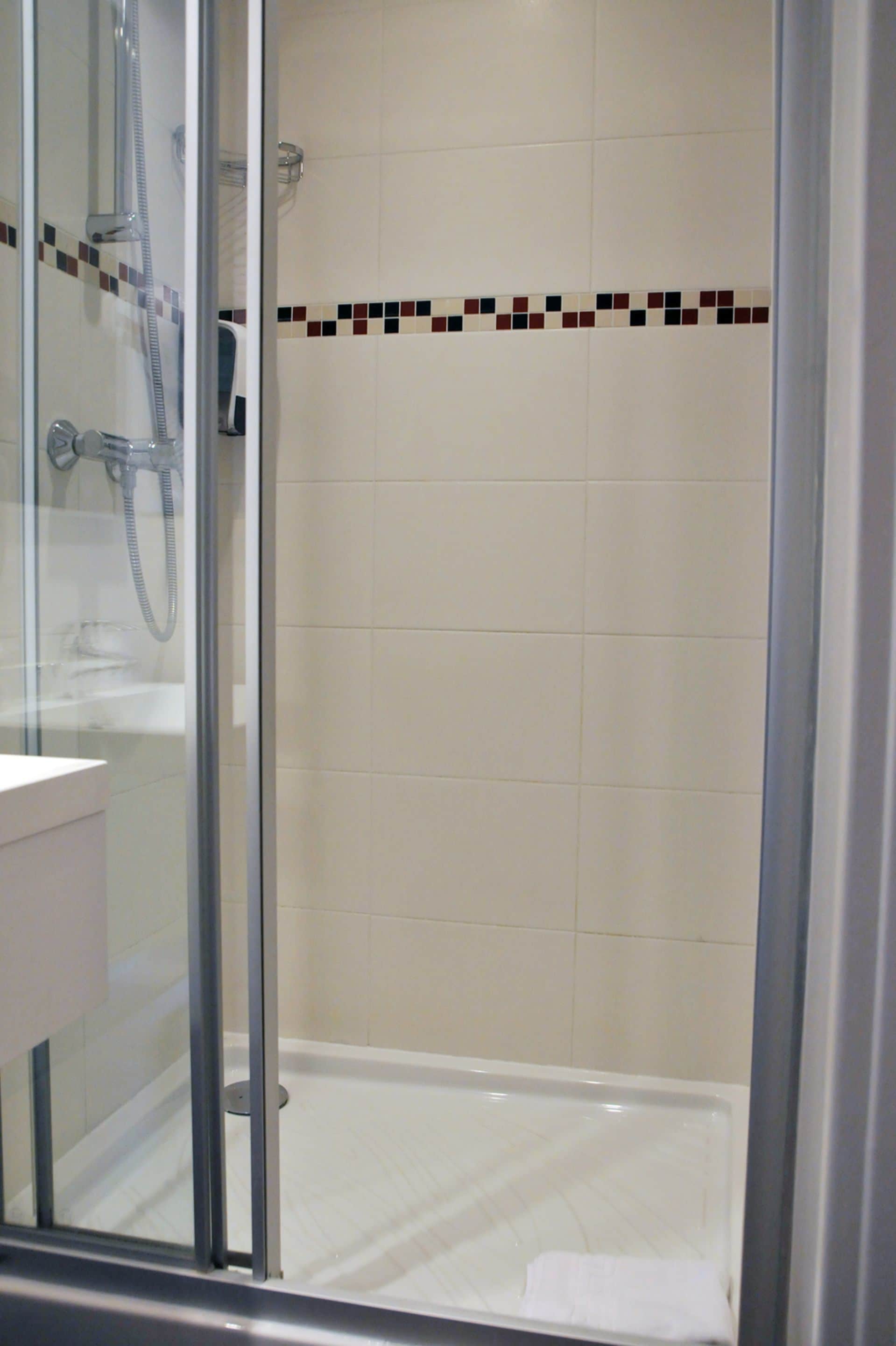 A glass-enclosed shower with a tiled floor and a small towel on the floor.