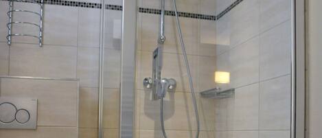 A glass-enclosed shower stall with a handheld showerhead and a handheld shower attachment.
