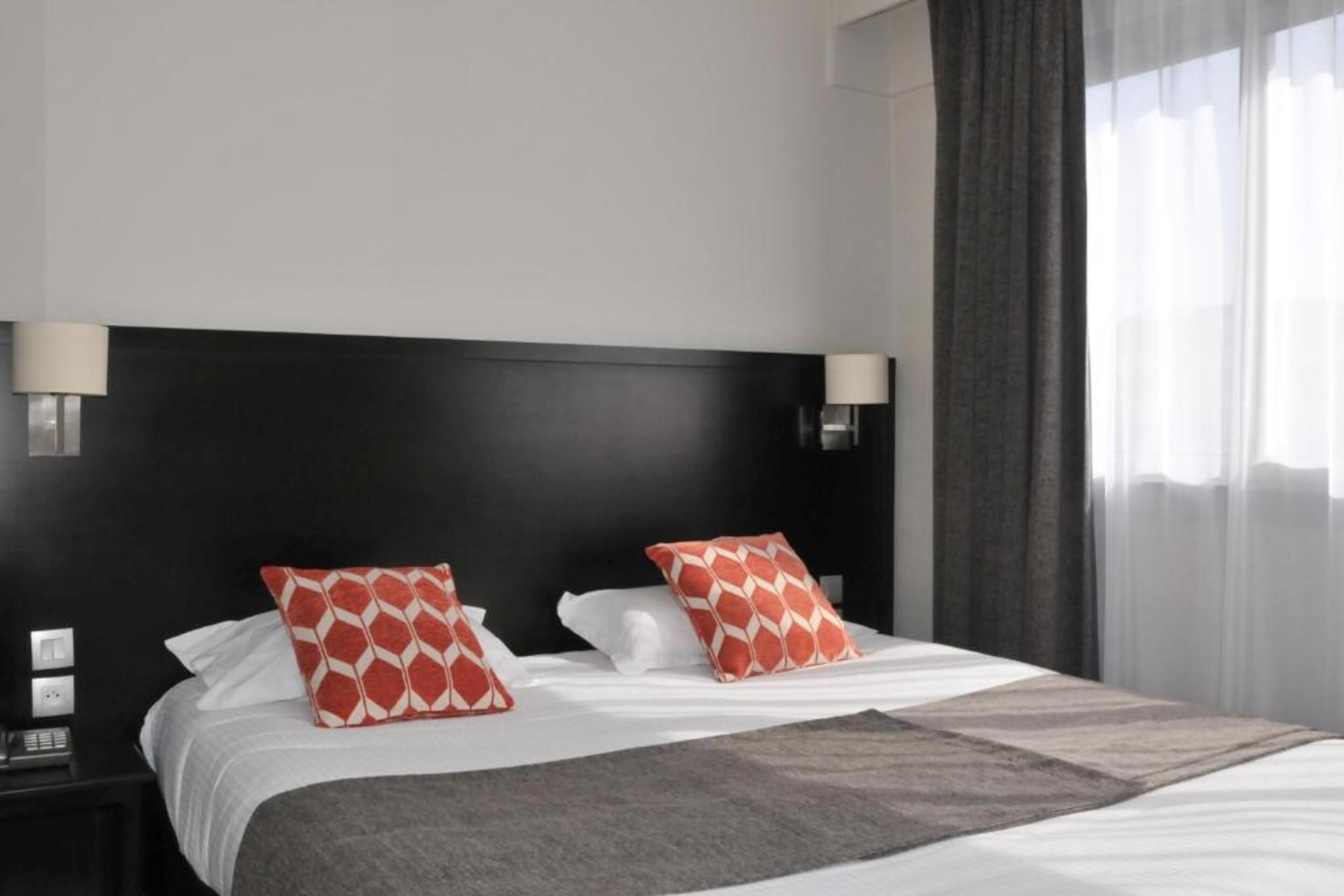 Una habitación de hotel con una cama, dos lámparas de noche, una mesita de noche y una ventana con cortinas.