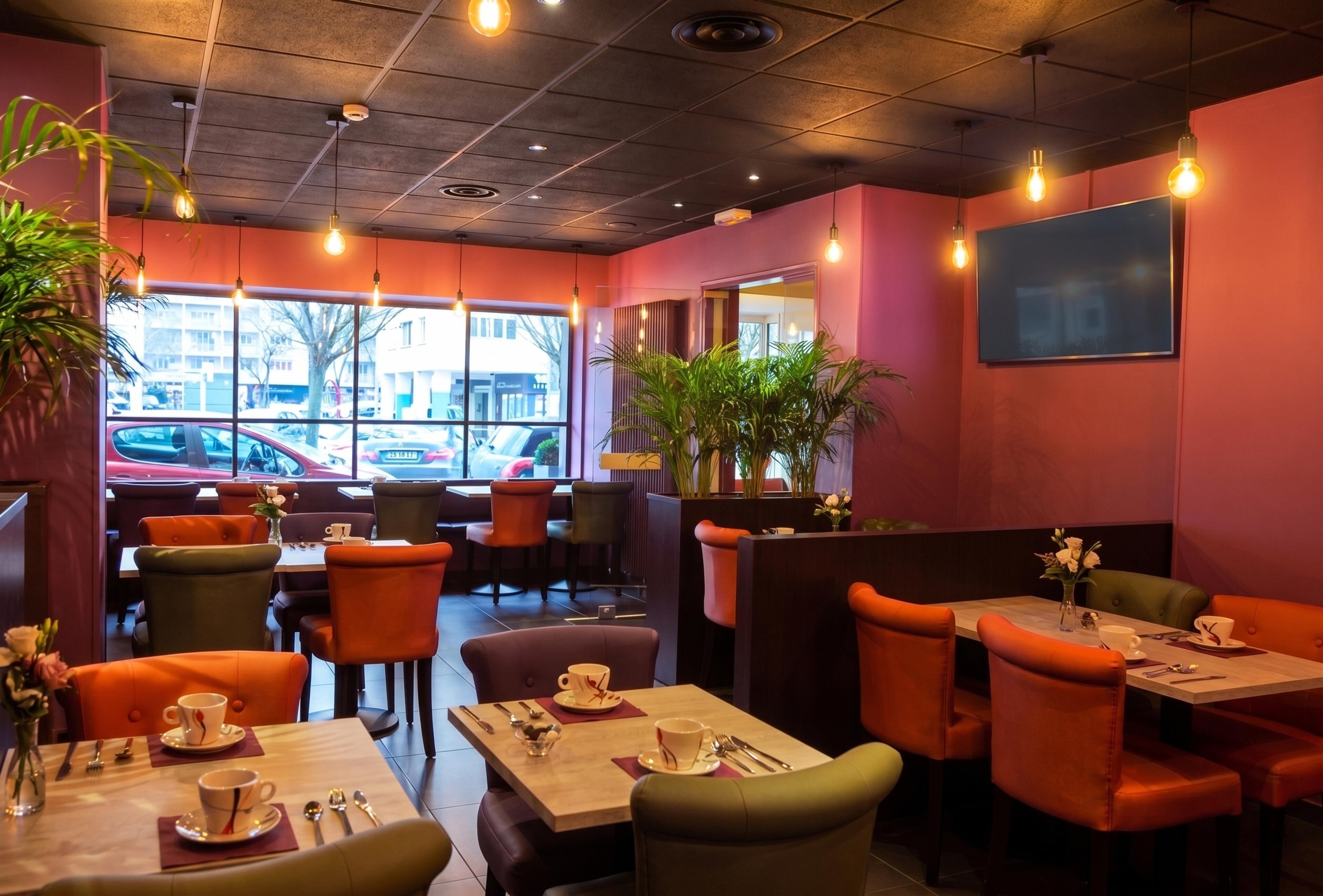 A restaurant interior with booths and tables, large windows with a view of parked cars, and hanging light fixtures.