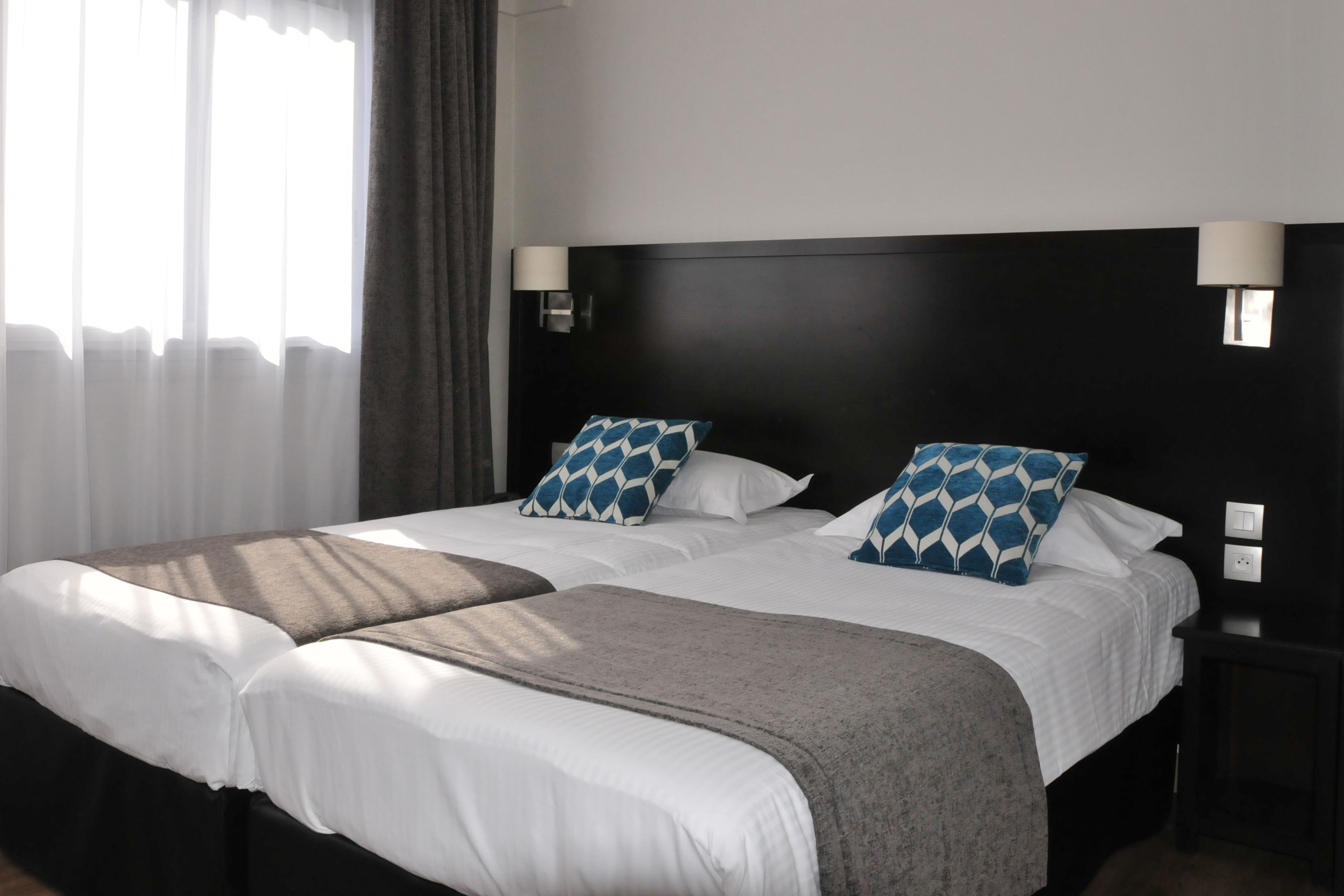 A hotel room with two beds, a dark headboard, bedside lamps, and a window with curtains.