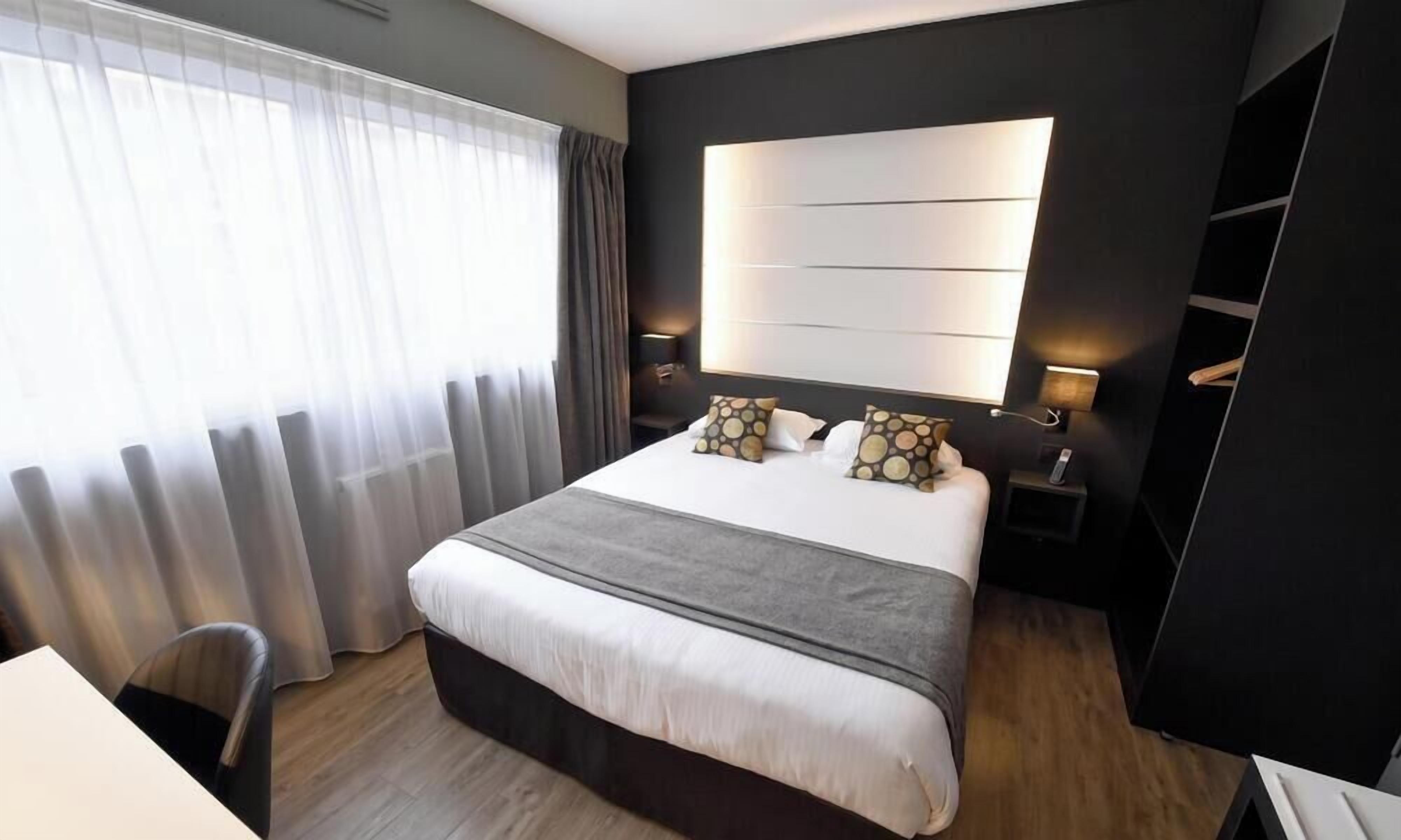 A modern hotel room with a large bed, bedside lamps, a desk, and a view of the outdoors.