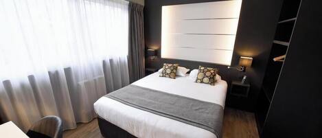 A modern hotel room with a large bed, bedside lamps, a desk, and a view of the outdoors.