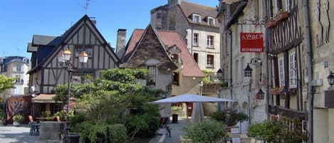 Una calle tradicional europea con edificios de entramado de madera, mesas al aire libre y un letrero de restaurante.