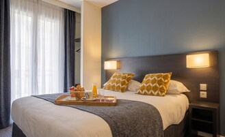 Habitación de hotel con cama, lámparas de noche, una bandeja con alimentos para el desayuno y una ventana con cortinas.