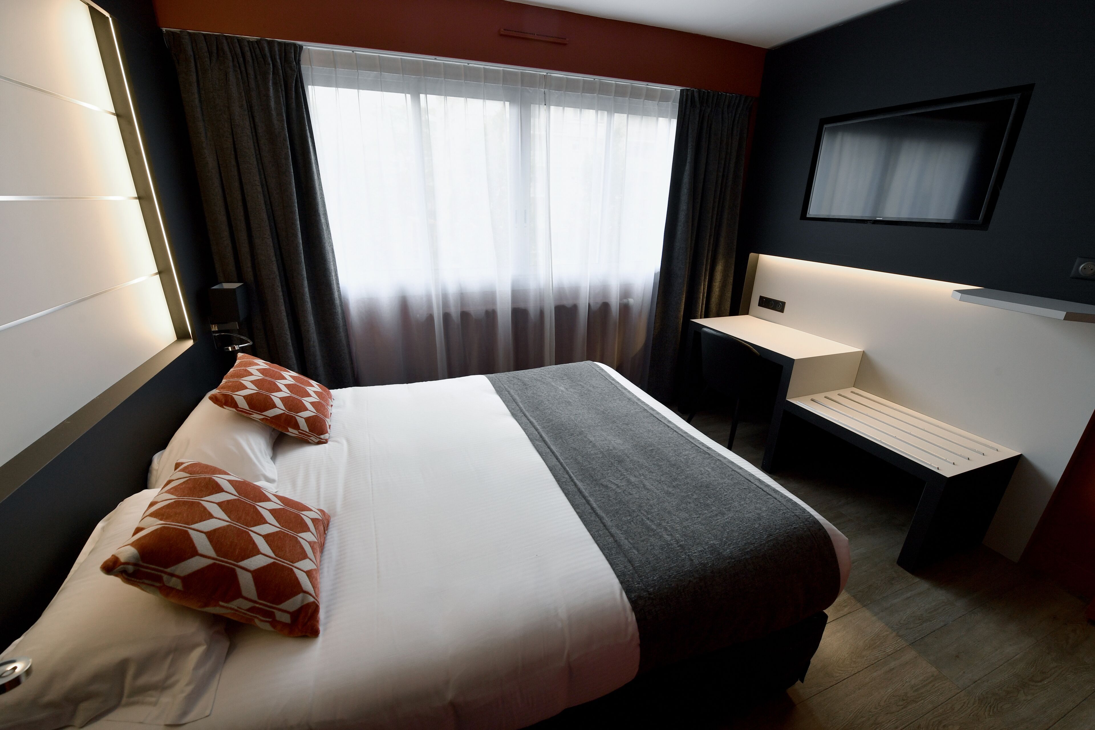 A hotel room with a bed, a desk, a chair, and a TV mounted on the wall.