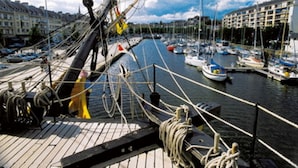 A marina with multiple boats docked, a ship's rigging, and buildings in the background. - Kyriad - Caen Centre (Caen)