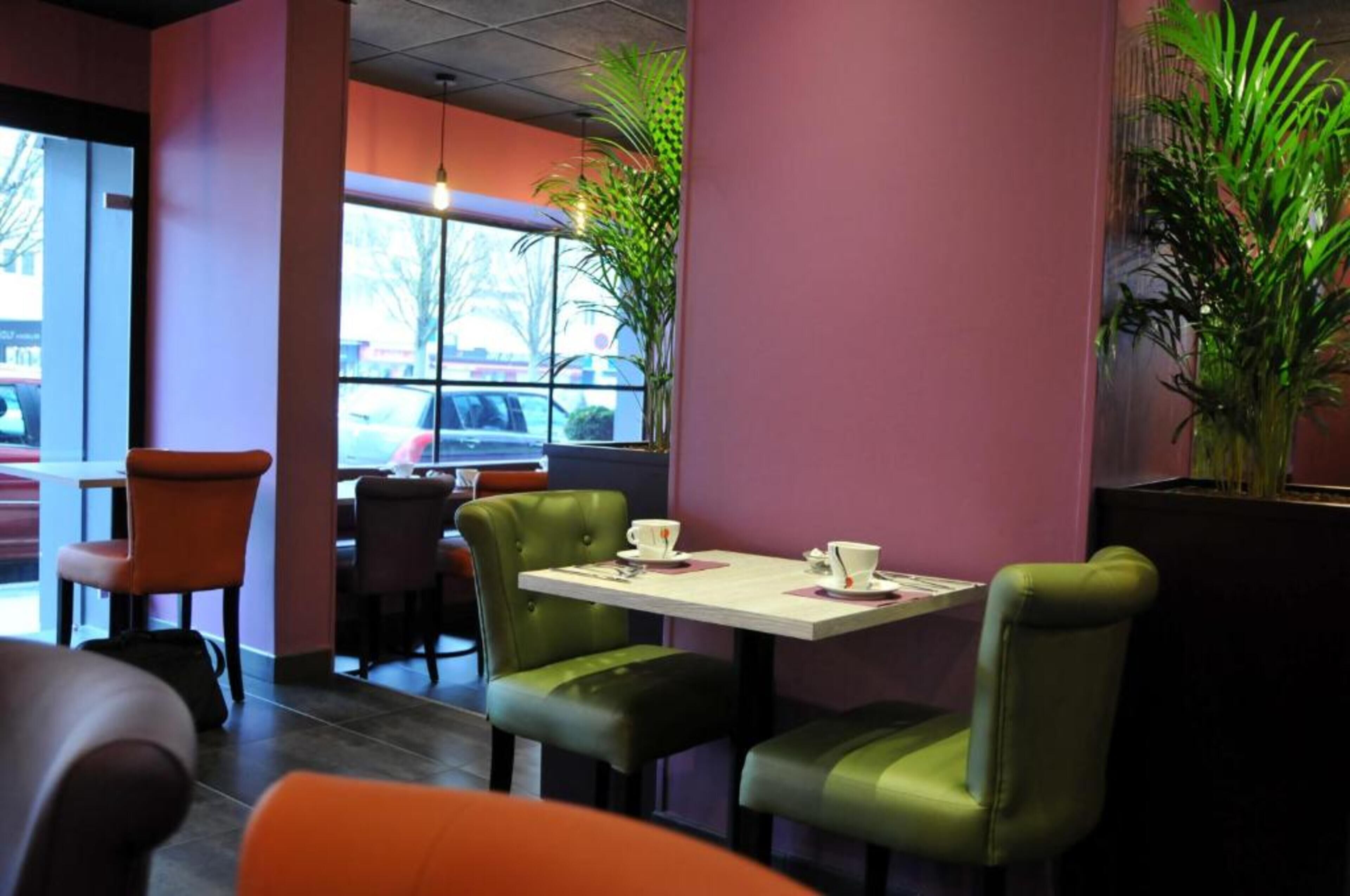 L’intérieur d’un restaurant, avec une table dressée pour deux personnes, des chaises vertes et une fenêtre donnant sur les voitures garées à l’extérieur.