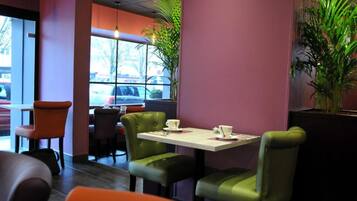 L’intérieur d’un restaurant, avec une table dressée pour deux personnes, des chaises vertes et une fenêtre donnant sur les voitures garées à l’extérieur.