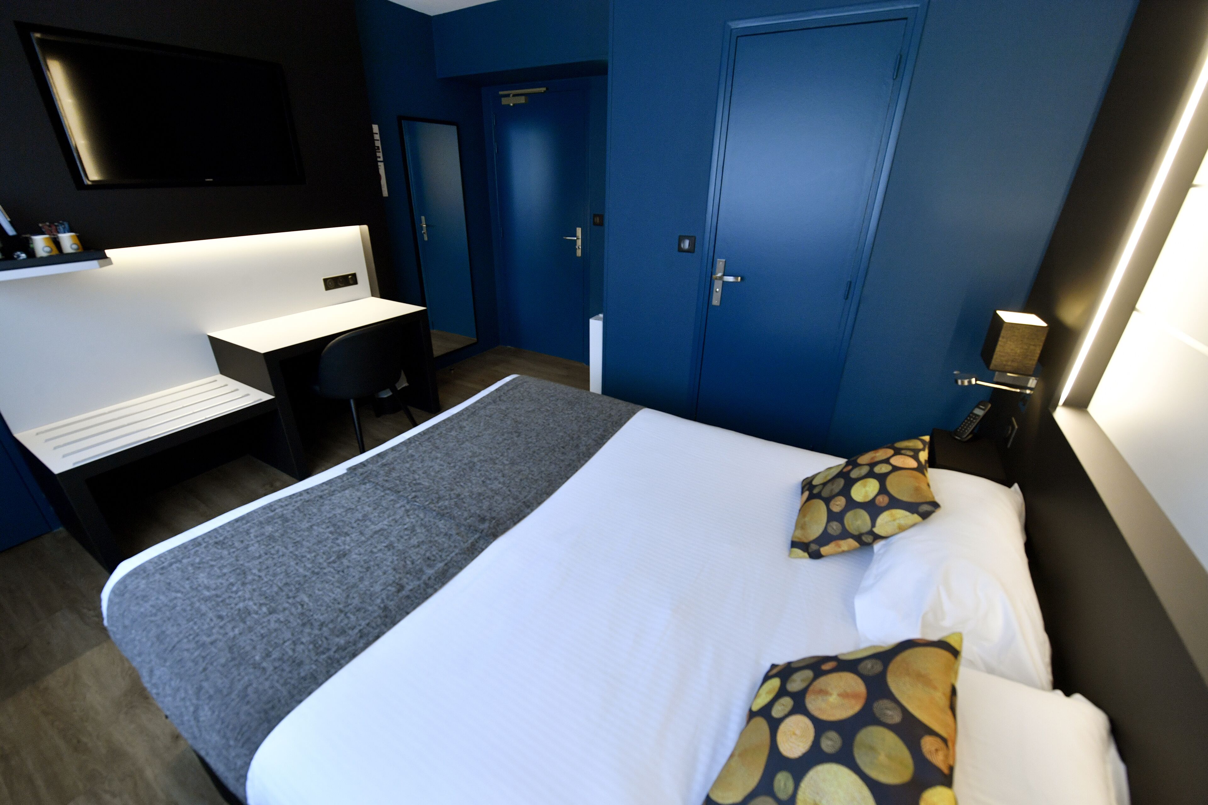 Habitación de hotel moderna con una cama grande, un escritorio y un televisor montado en la pared.