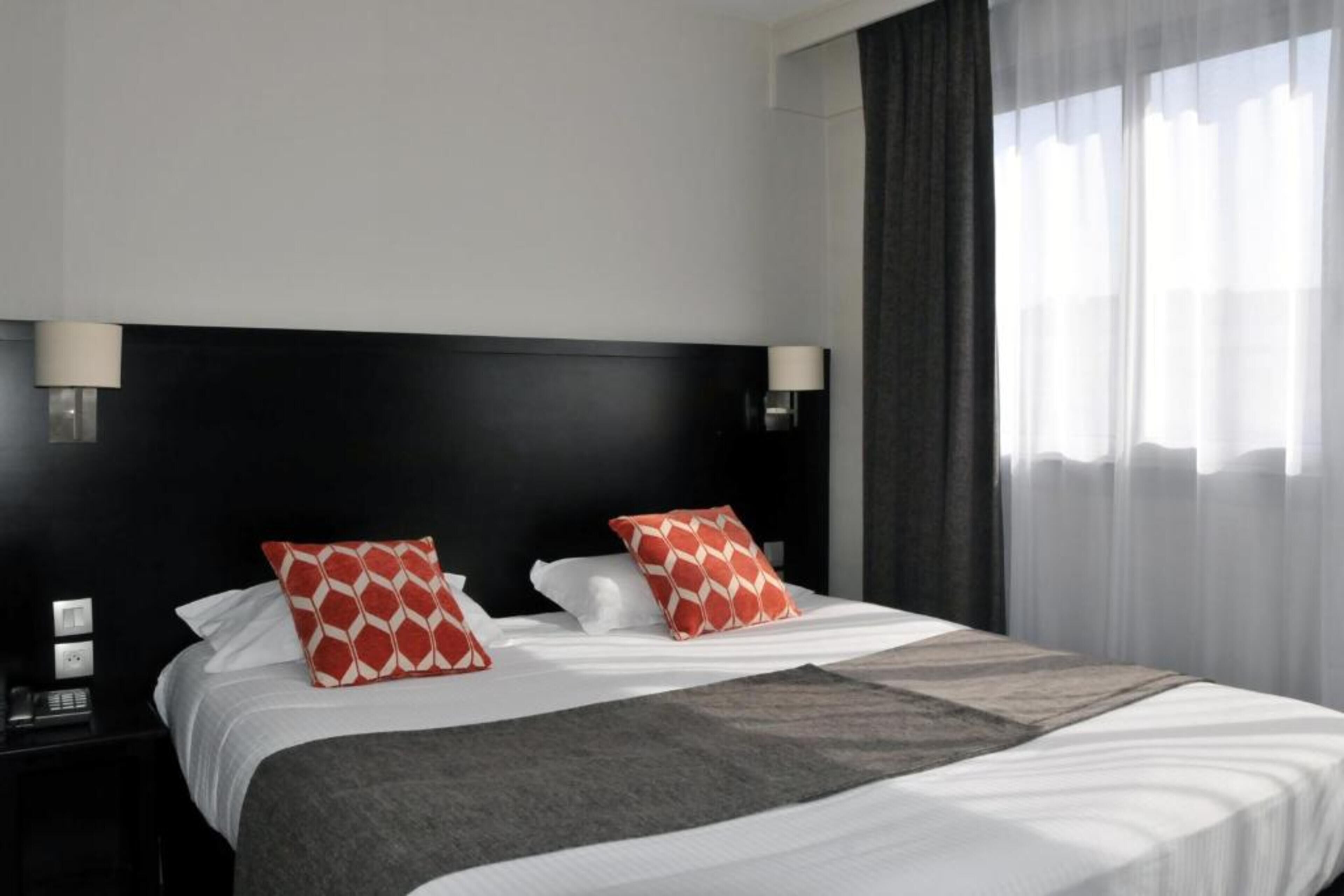 A hotel room with a large bed, two bedside lamps, and a view of the outside through sheer curtains.
