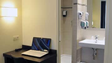 A hotel room with a desk, chair, laptop, shower, and sink.