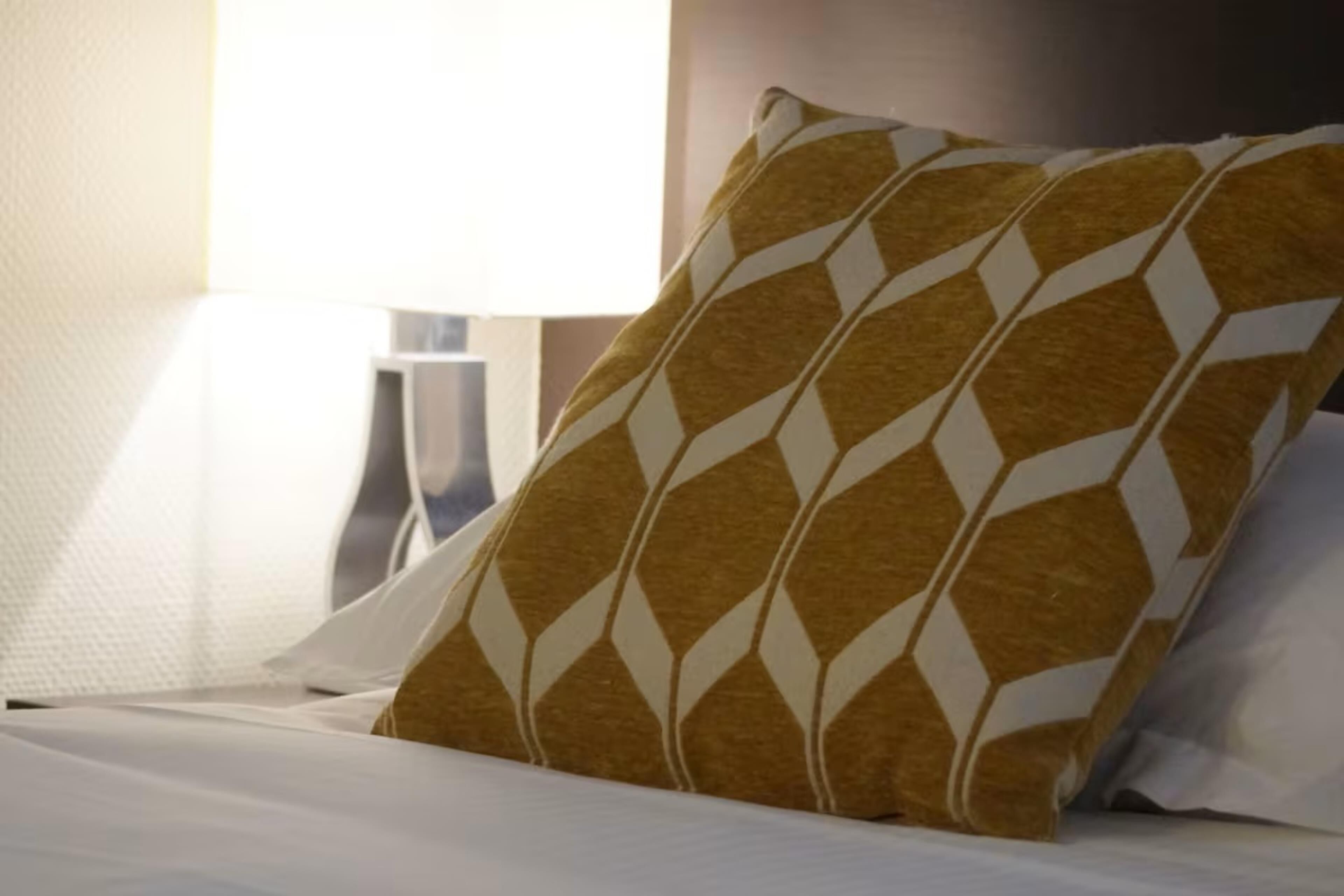A bed with a patterned pillow and a plain pillow, a bedside table, and a lamp.