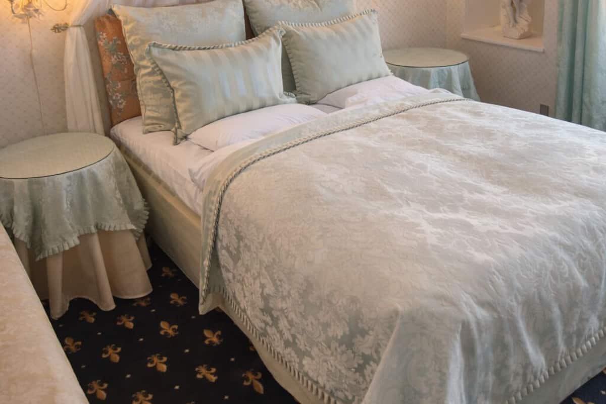 A bedroom with a canopy bed, two bedside tables, a nightstand, a wall-mounted mirror, and a statue.