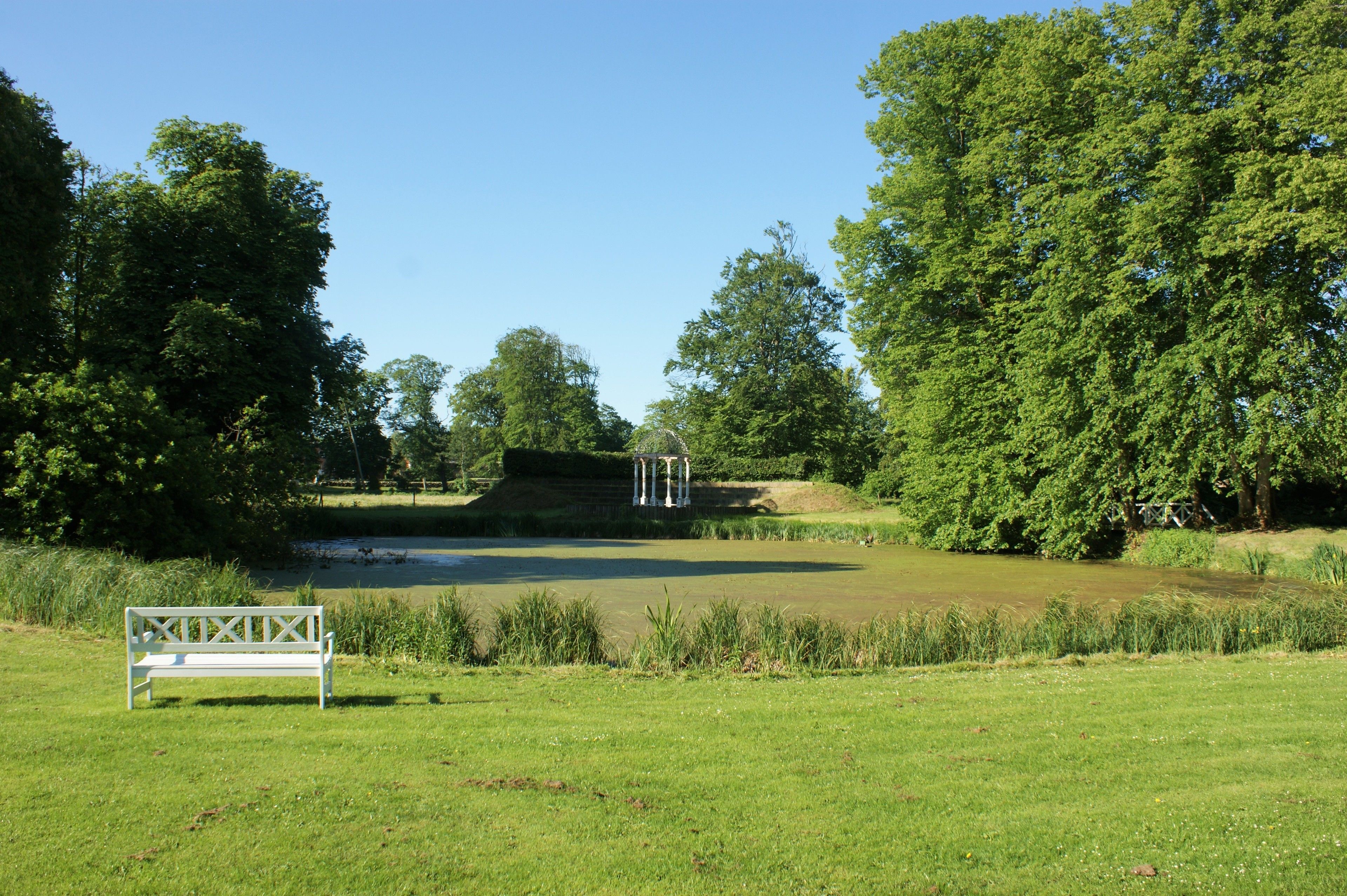 A park with a white bench, a pond, and a gazebo.